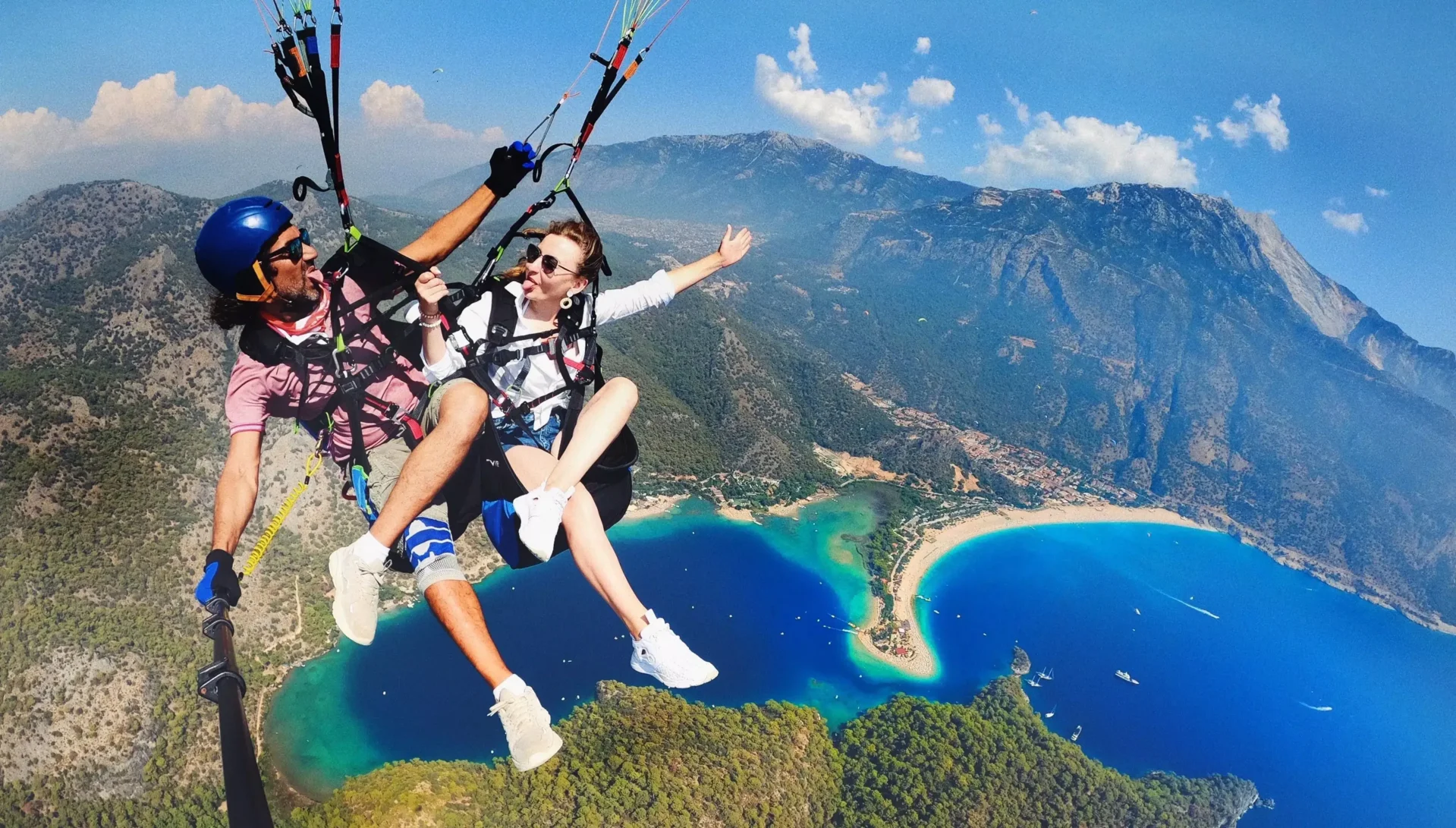Bild Gleitschirm: Beratung BU - Junges Paar fliegt Tandem-Gleitschirm über malerischer Strandkulisse und macht Selfie